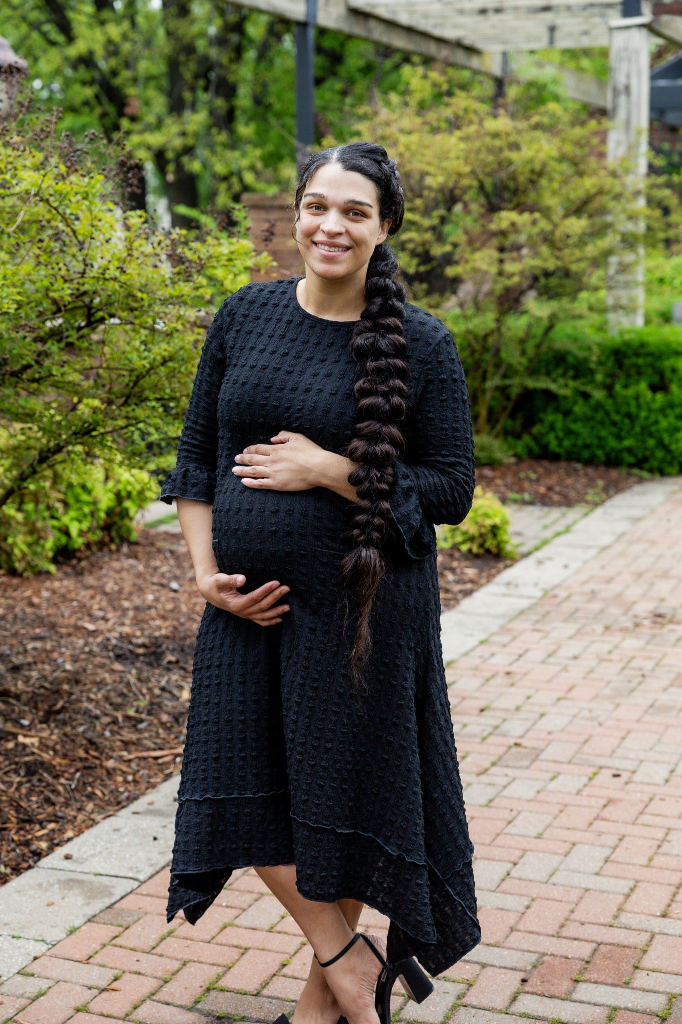 Women wearing a black modest, midi length dress that is maternity friendly.
