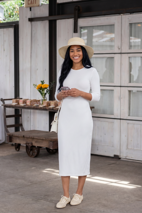Woman in a white dress and hat standing in front of a rustic wooden door.