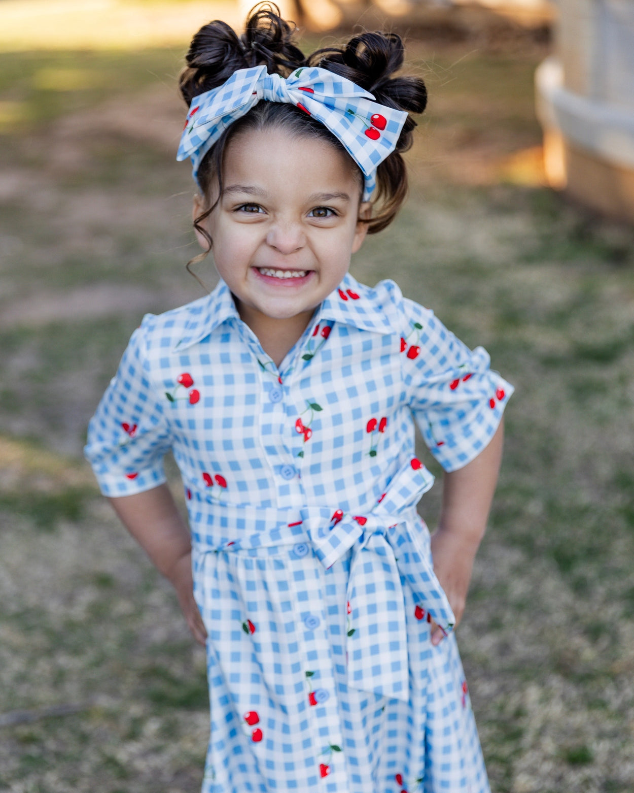 Model wearing the Nuggles® Girls' Rachel Dress and headband in Sweet Cherry Check