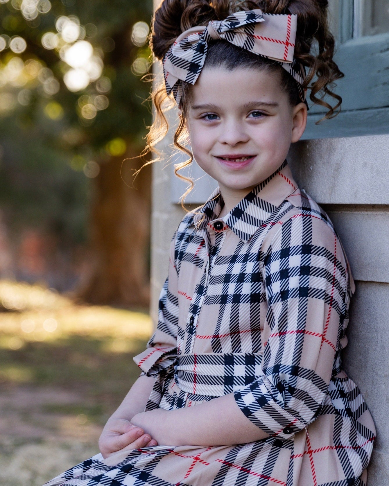 Model wearing the Nuggles® Girls' Rachel Dress and matching Headband in Sand Plaid