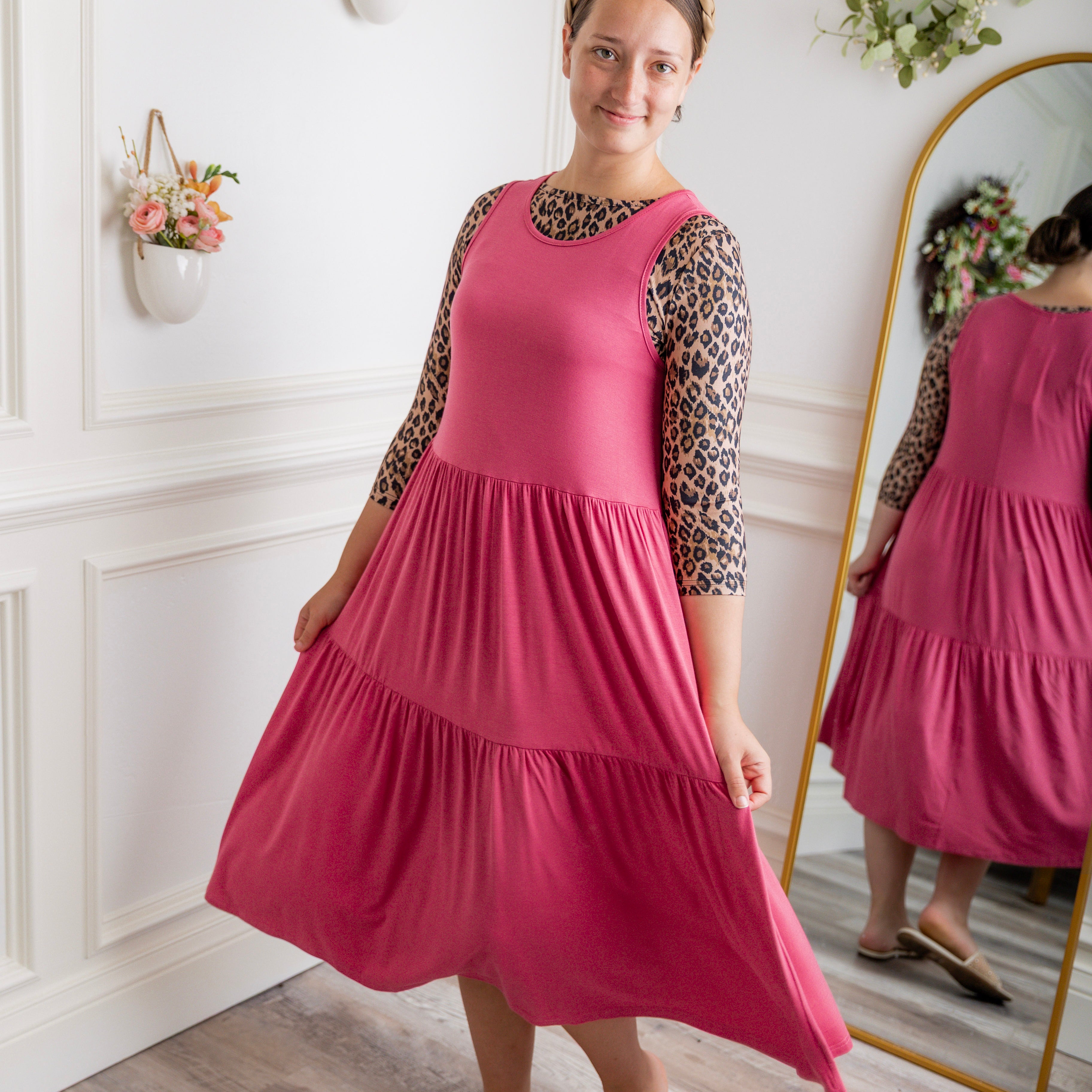 model modeling a pink tiered midi dress over a leopard print sleeve top, styled with nude studded sandals and a braided headband.