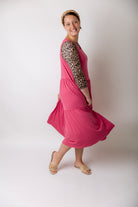 model modeling a pink tiered midi dress over a leopard print sleeve top, styled with nude studded sandals and a braided headband.