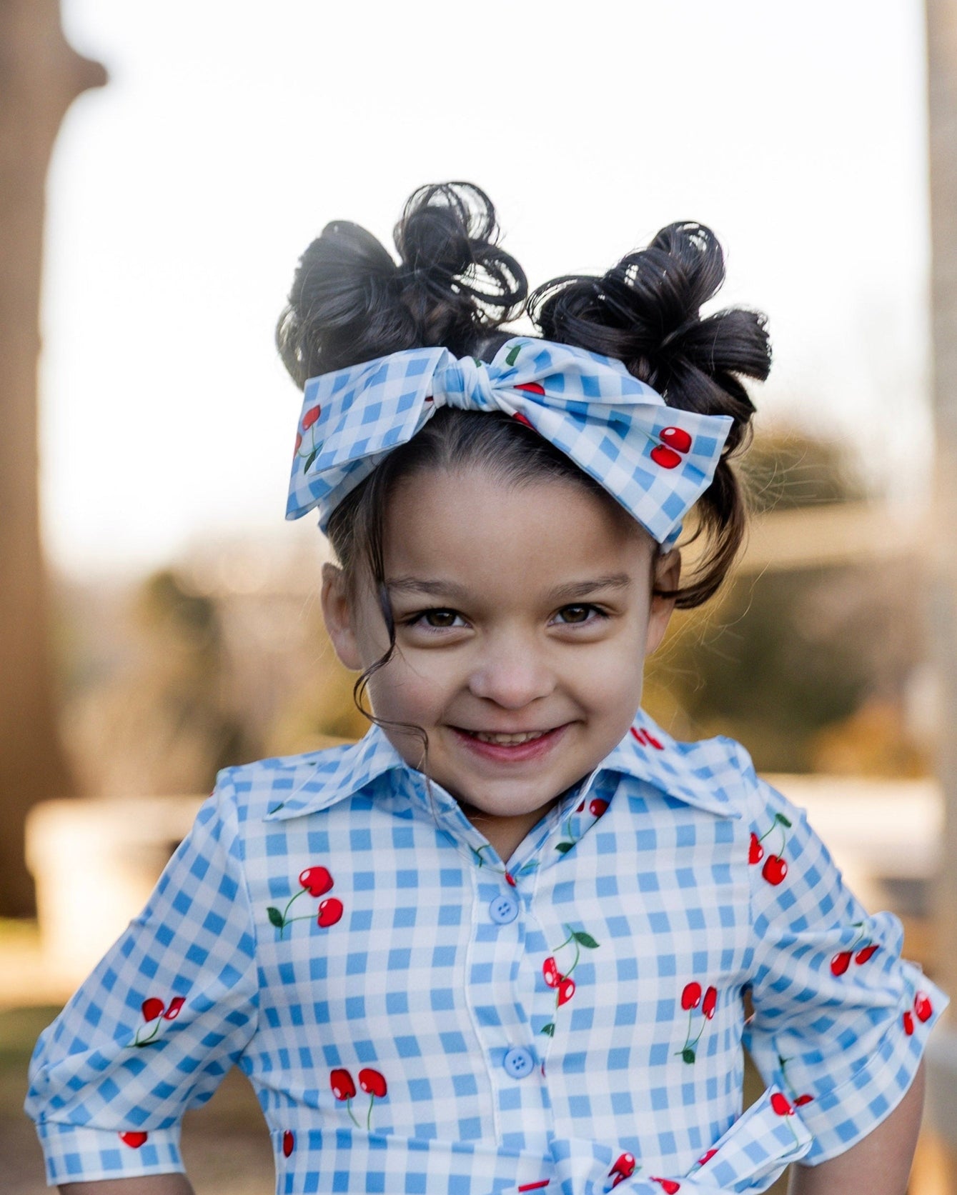 Model wearing the Nuggles® Girls' Rachel Dress and headband in Sweet Cherry Check