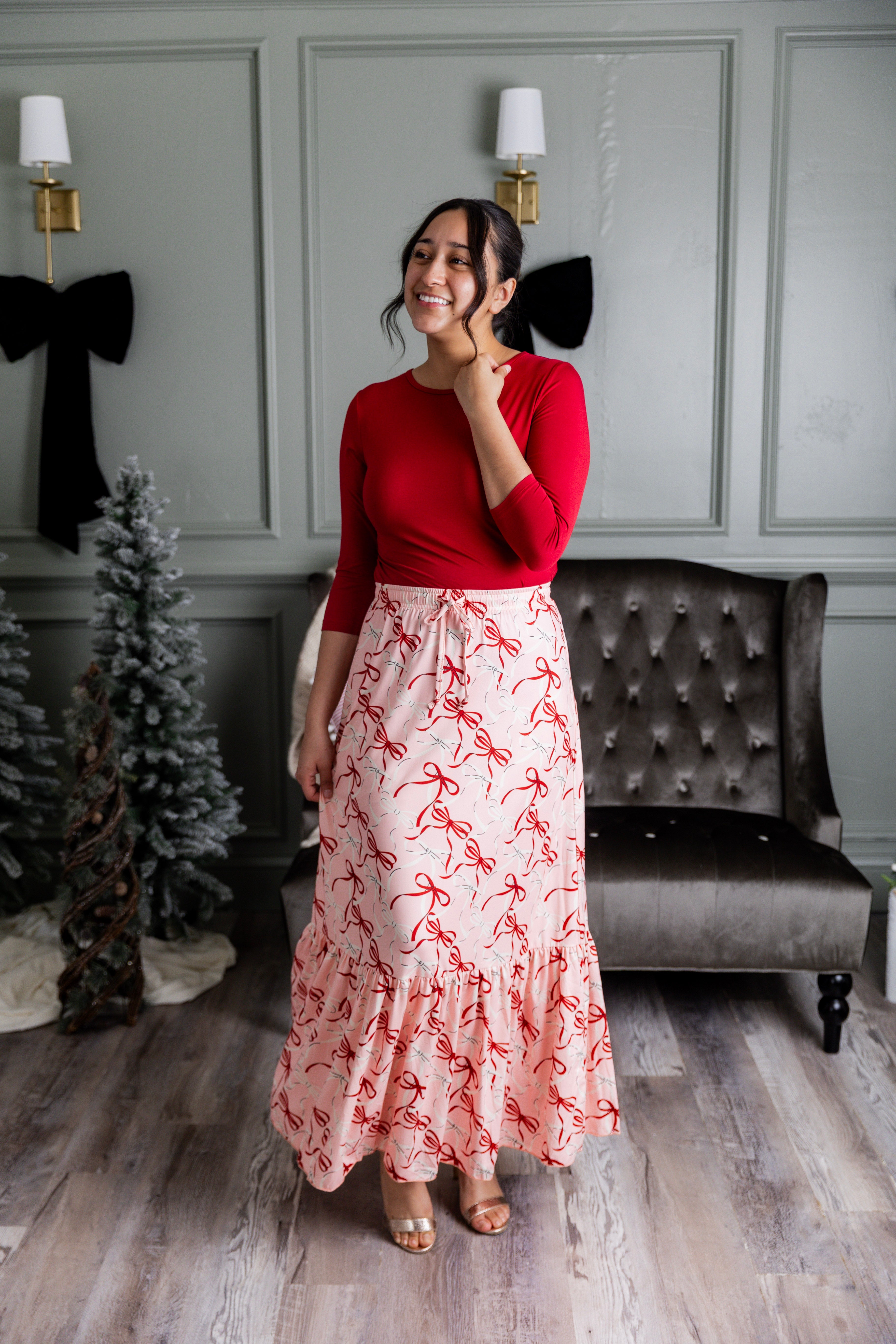 Model wearing the Nuggles® Sage Skirt in pink with red bow print, showcasing a tiered ruffle hem and soft, stretchy waistband.