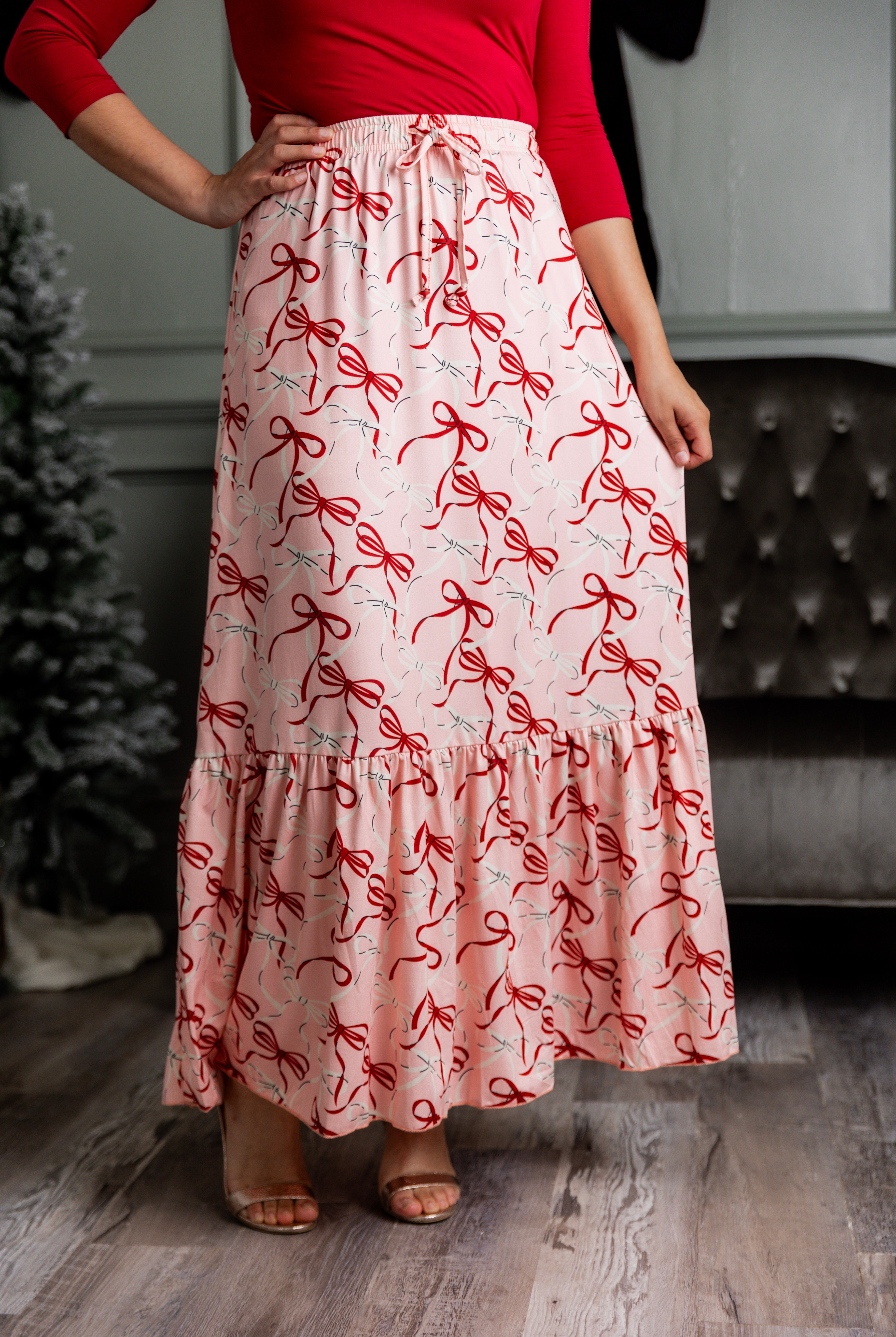 Model wearing the Nuggles® Sage Skirt in pink with red bow print, showcasing a tiered ruffle hem and soft, stretchy waistband.