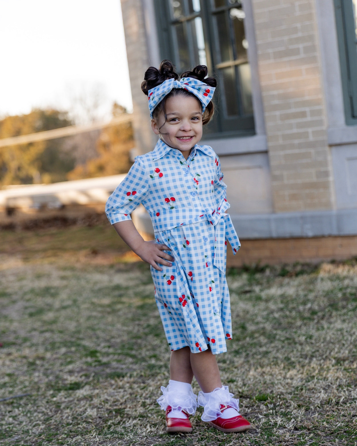Model wearing the Nuggles® Girls' Rachel Dress and headband in Sweet Cherry Check