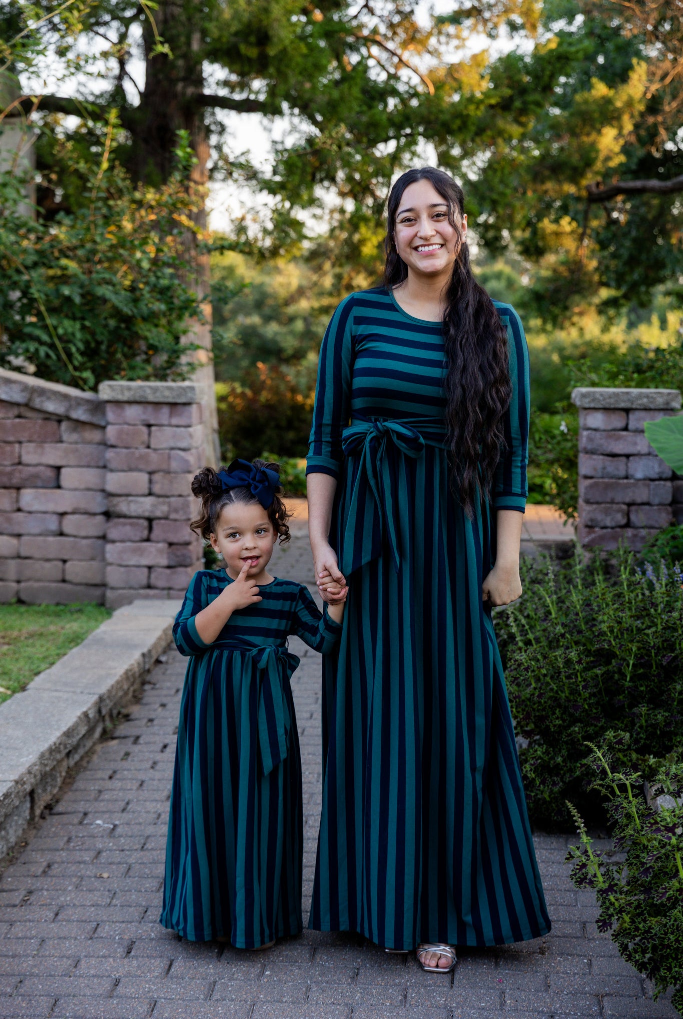 Young girl wearing the Nuggles® Girls Adelia Dress — a modest striped maxi dress with bow tie waist.