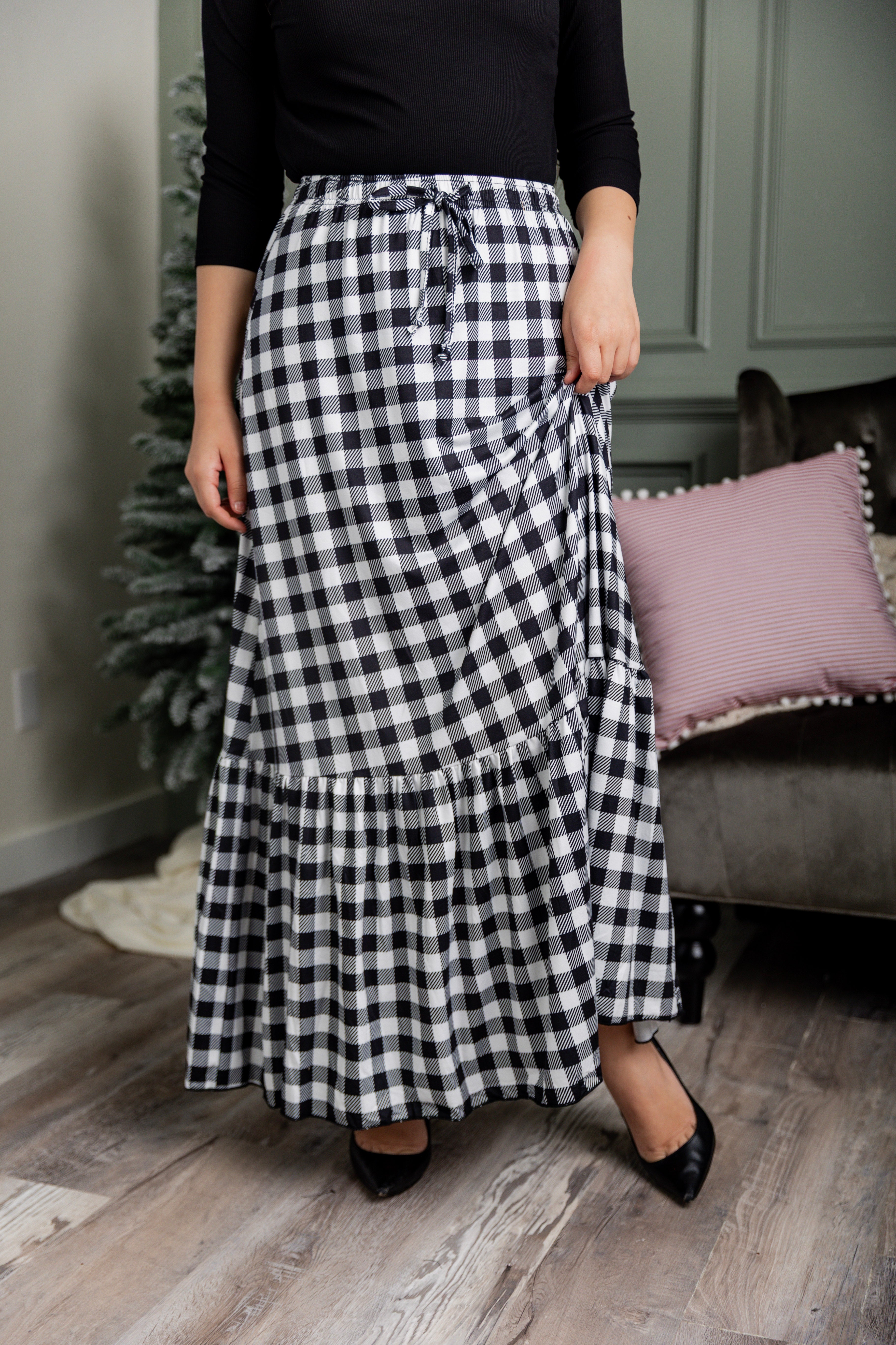 Model wearing the Nuggles® Sage Skirt in black and white gingham, featuring a tiered ruffle hem and drawstring waist.