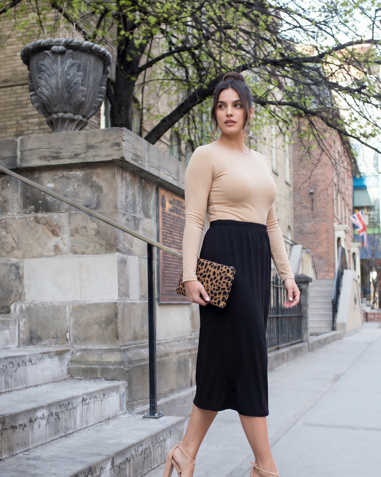 Woman in beige top and black skirt standing on a city street.