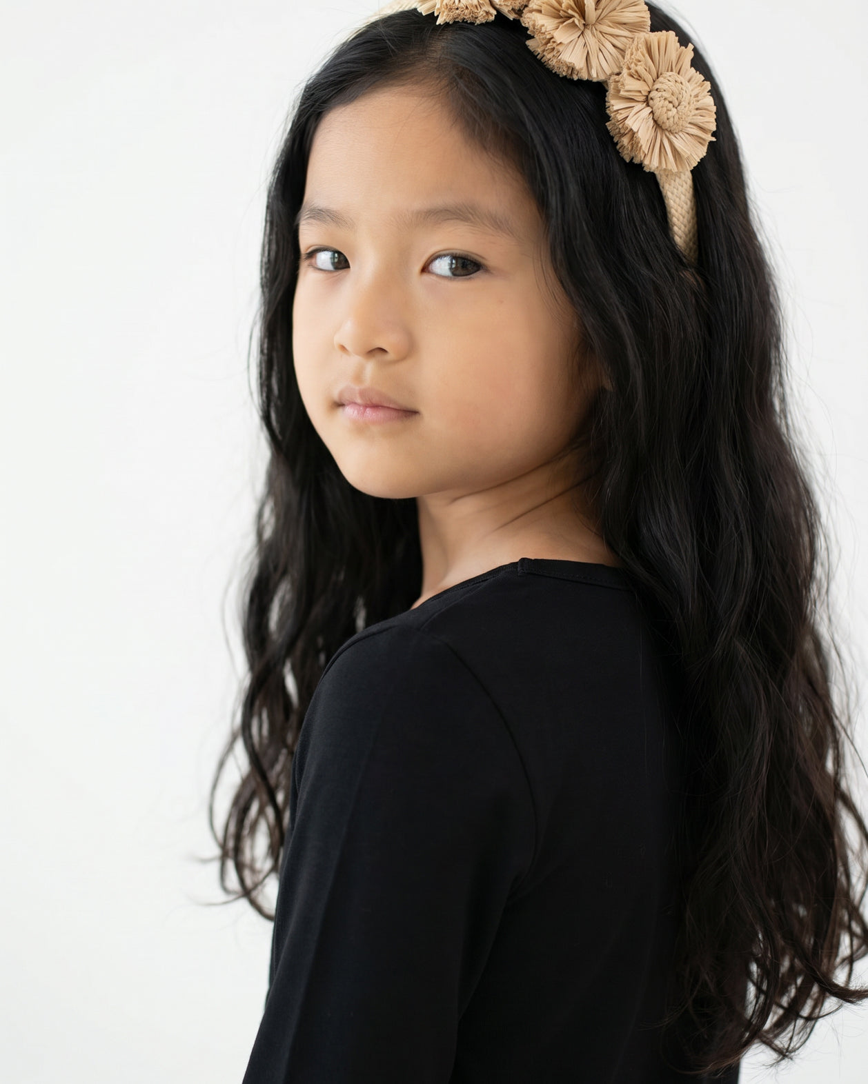 Young girl with long dark hair wearing Nuggles® Black Tee and a beige floral headband against a white background.
