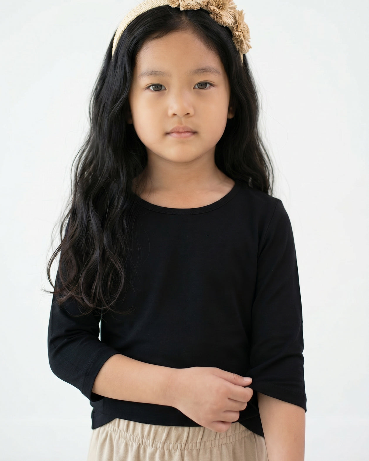 Young girl with long dark hair wearing Nuggles® Black Tee and a beige floral headband against a white background.
