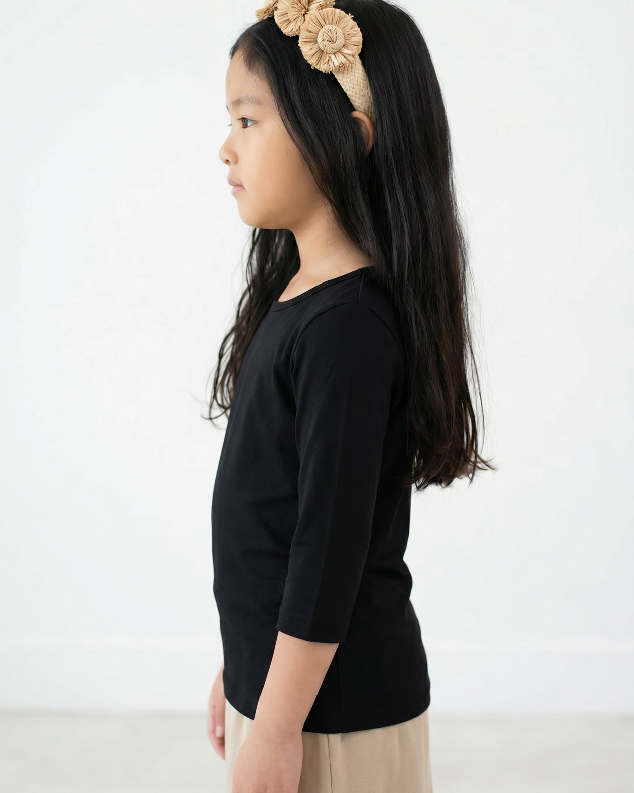 Young girl with long dark hair wearing Nuggles® Black Tee and a beige floral headband against a white background.