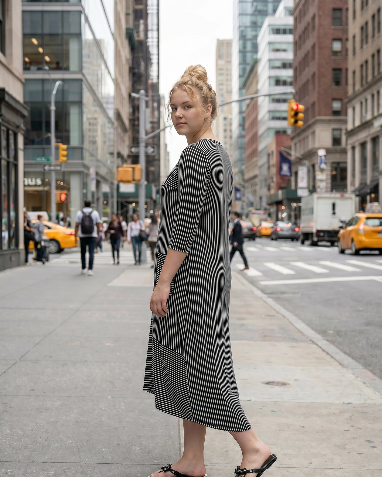 Woman in a black and white striped dress standing on a city street.