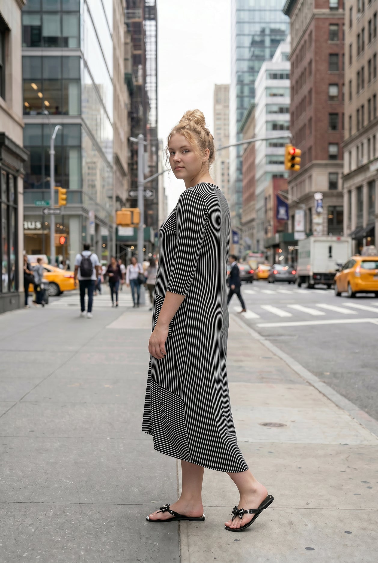 Woman in a black and white striped dress standing on a city street.