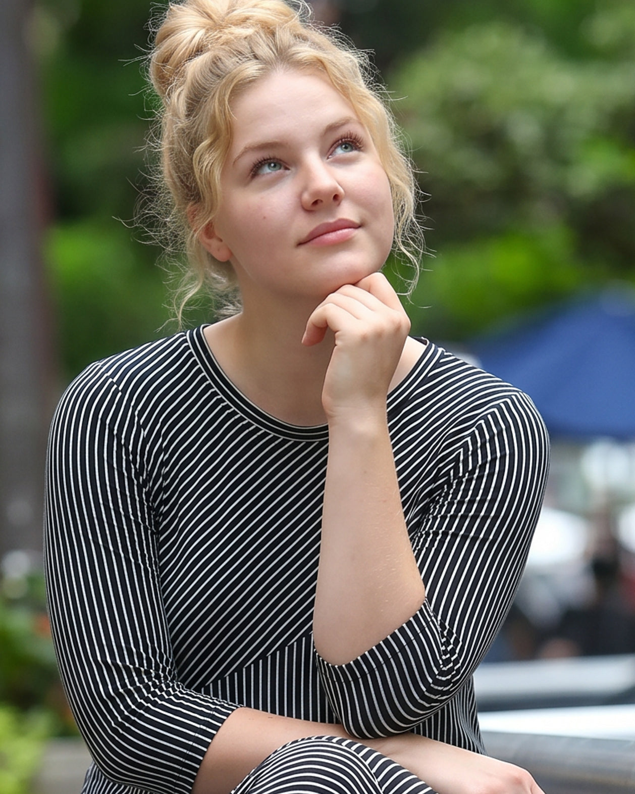 Woman in a striped dress sitting outdoors with trees in the background