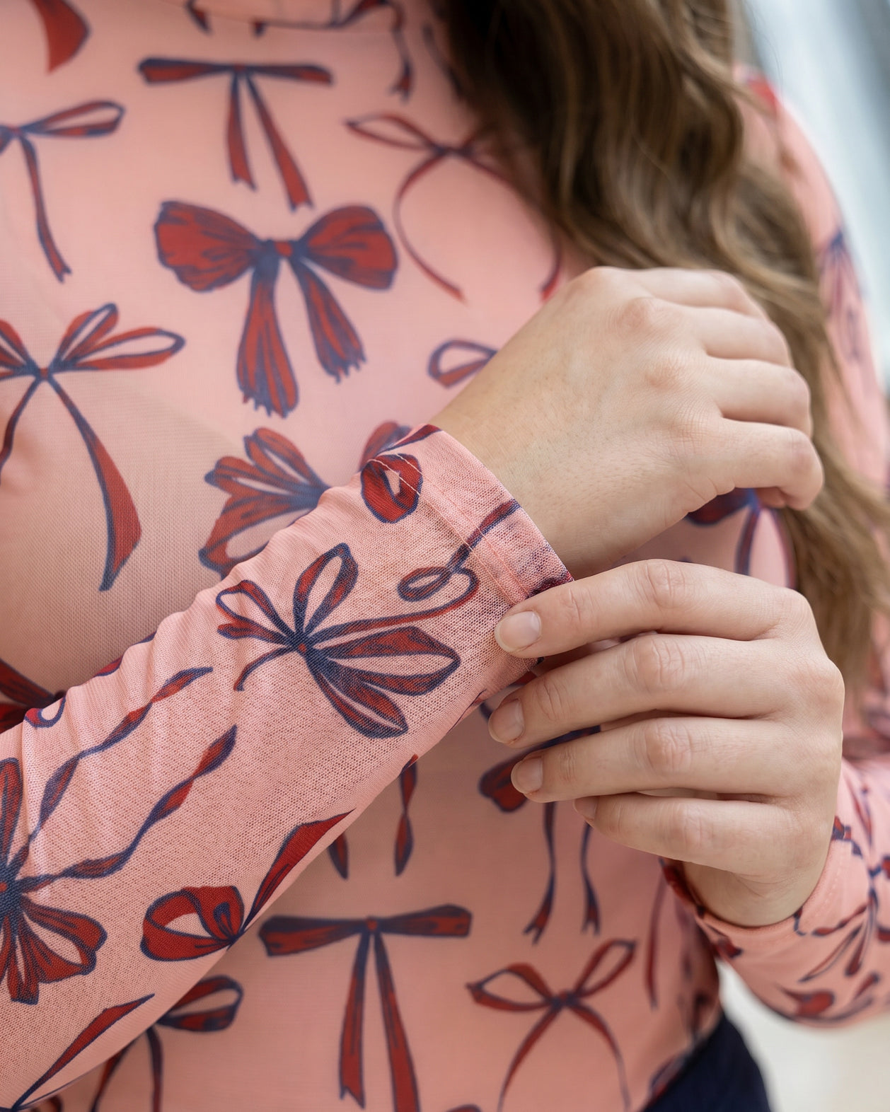 A picture of a women wearing a pink, red, and blue bow print mesh tee.