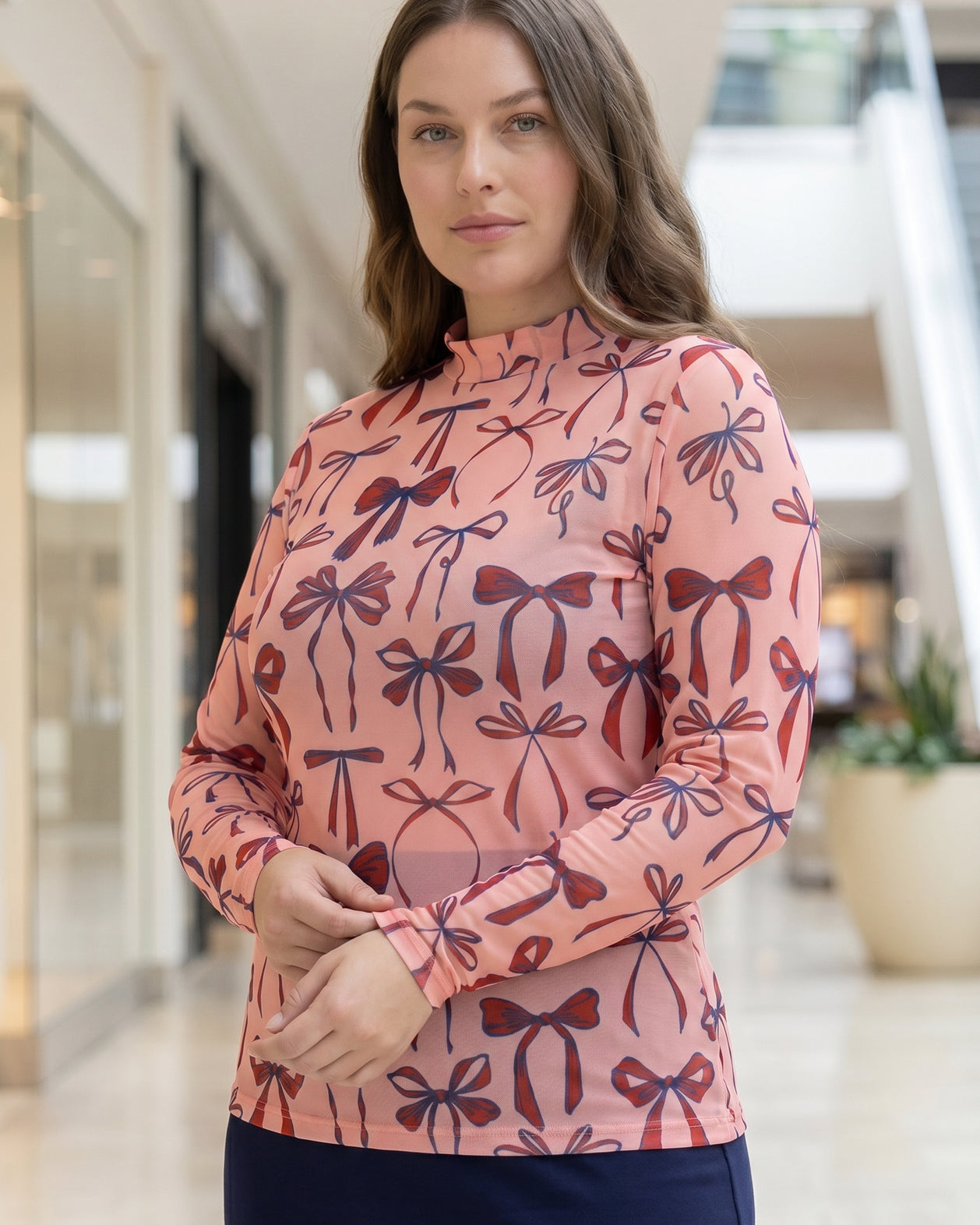 A picture of a women wearing a pink, red, and blue bow print mesh tee.