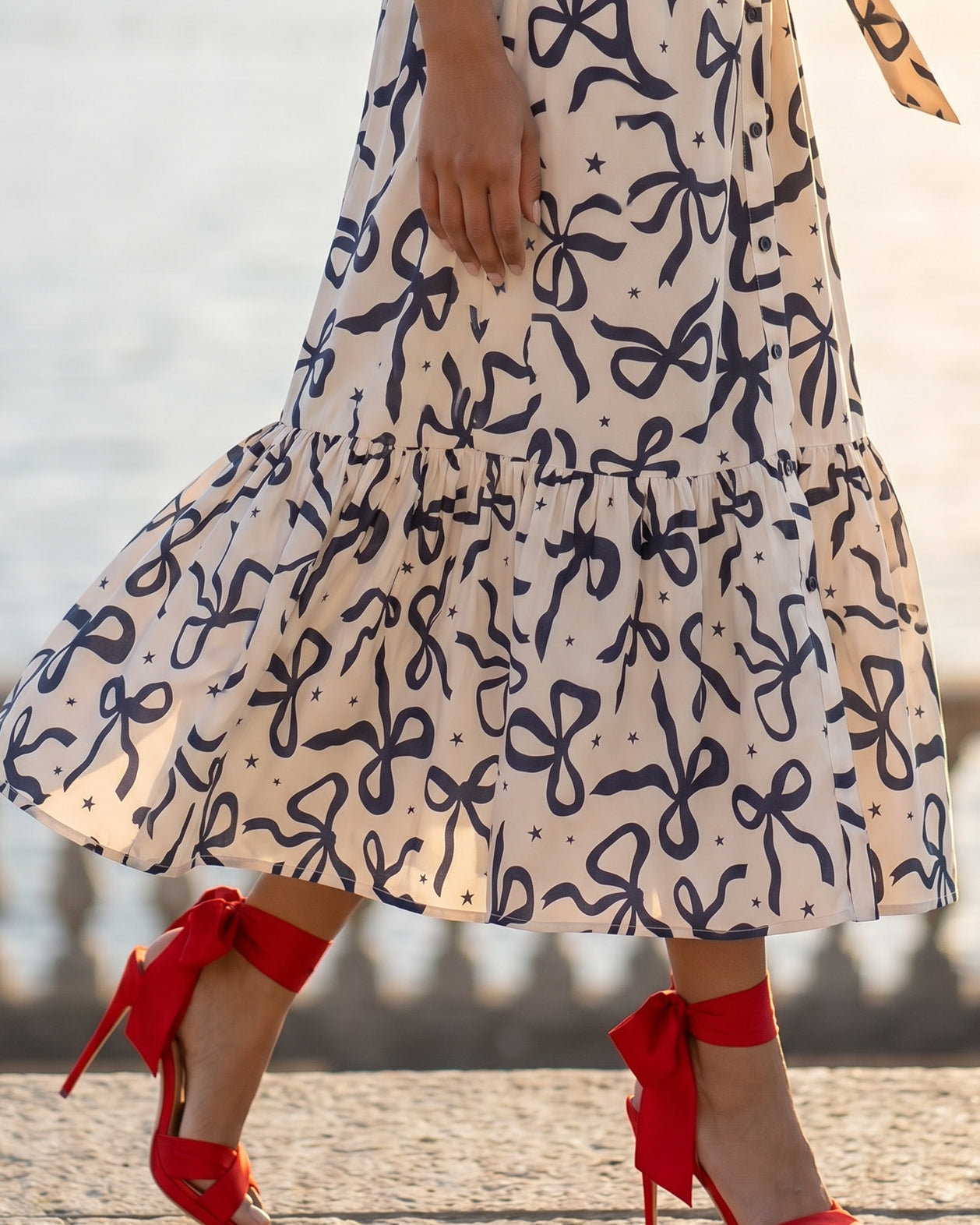 A picture of a young women wearing the Leila Dress in a bow print with a soft ivory base.