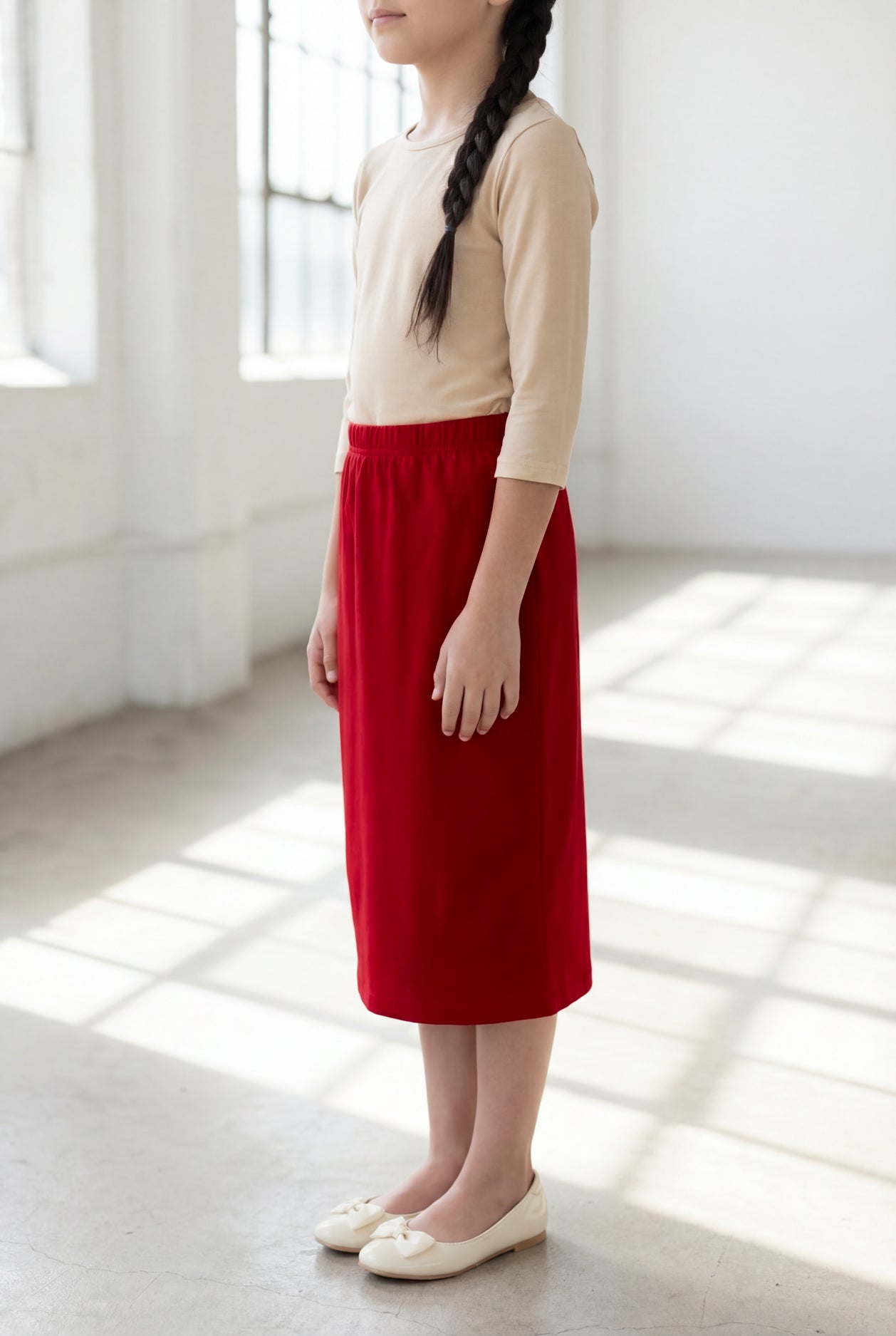 Girl wearing Nuggles® Modest Midi Skirt in Brick Red with a nude essential 3/4 tee in a sun light loft