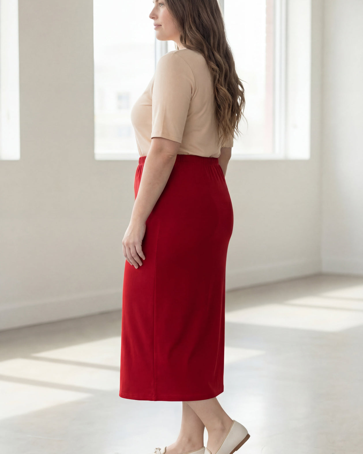 Woman wearing a red skirt and beige top in a bright room with large windows.