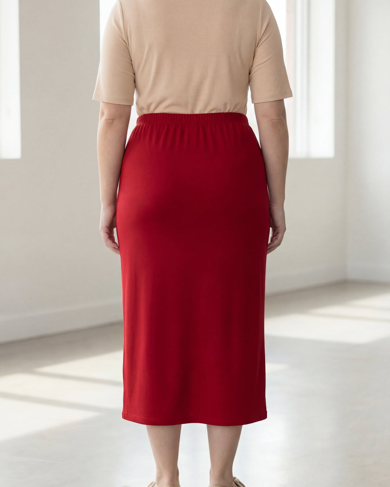 Person wearing a beige top and red skirt in a bright room.