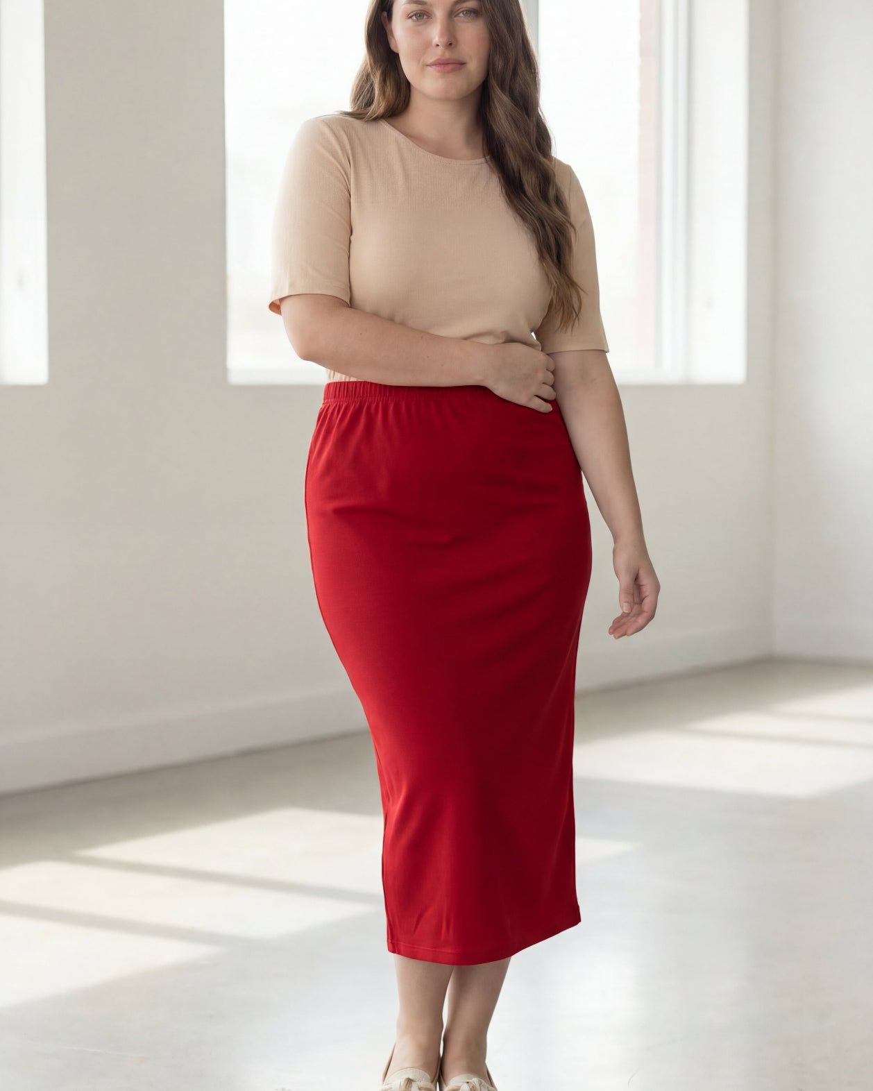 Woman wearing a beige top and red skirt in a bright room.