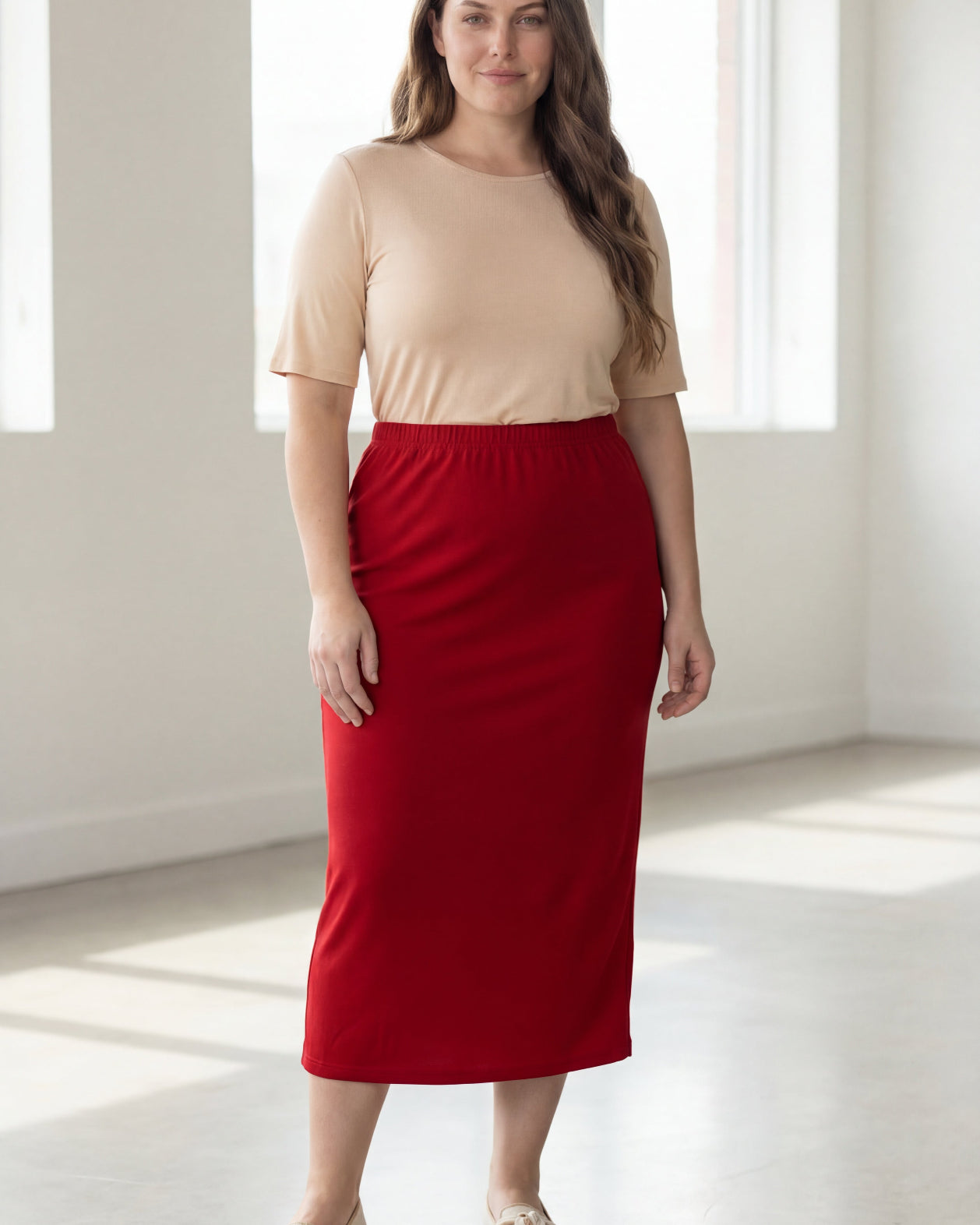 Woman wearing a beige top and red skirt in a bright room.