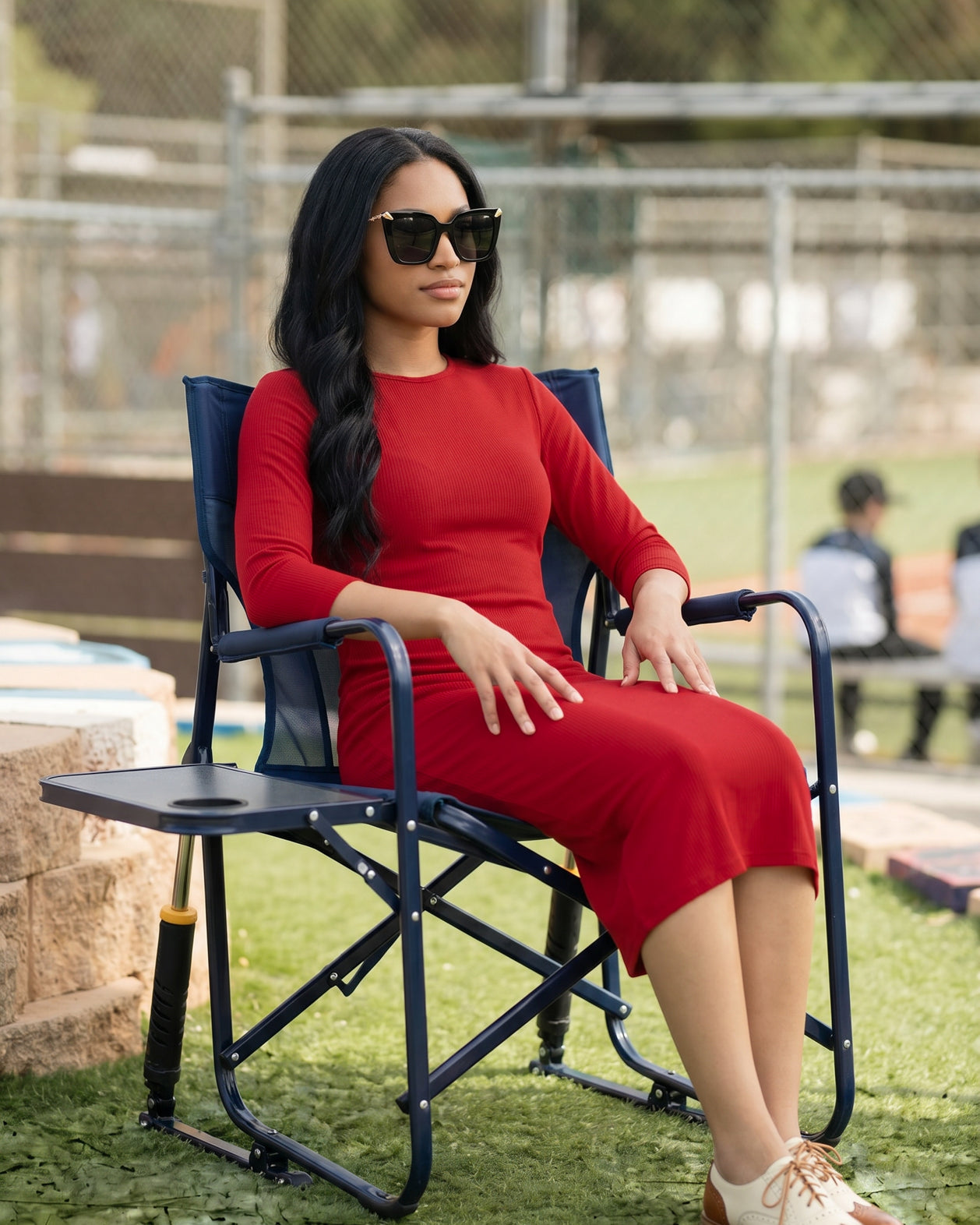 Woman in a red dress sitting on a folding chair outdoors.