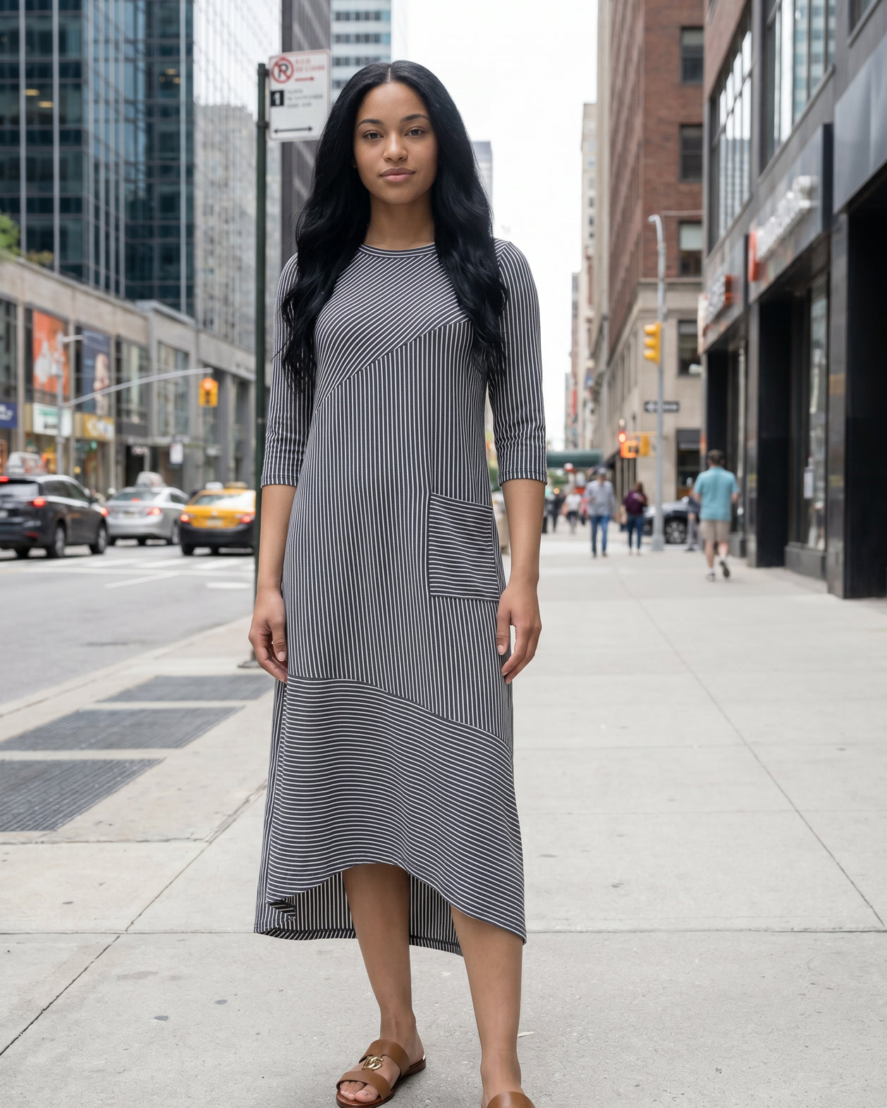 Woman in a gray dress standing on a city street with tall buildings in the background.
