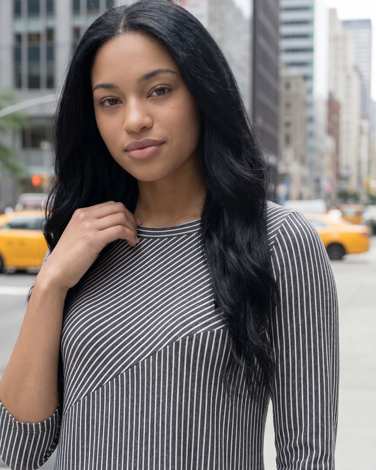 Woman in a gray dress standing on a city street with tall buildings in the background.