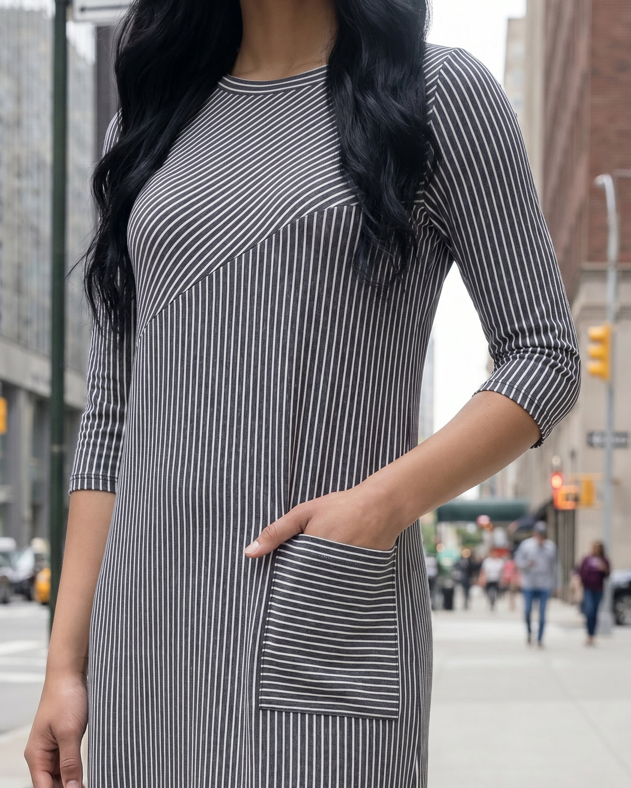 Woman in a gray dress standing on a city street with tall buildings in the background.