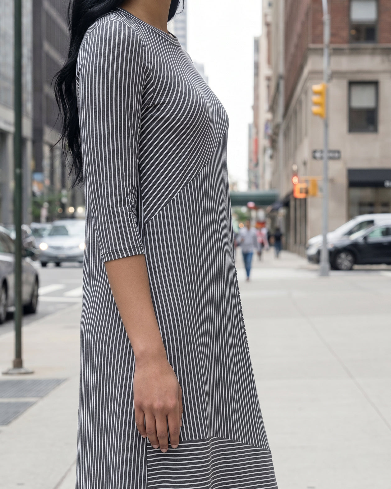 Woman in a gray dress standing on a city street with tall buildings in the background.