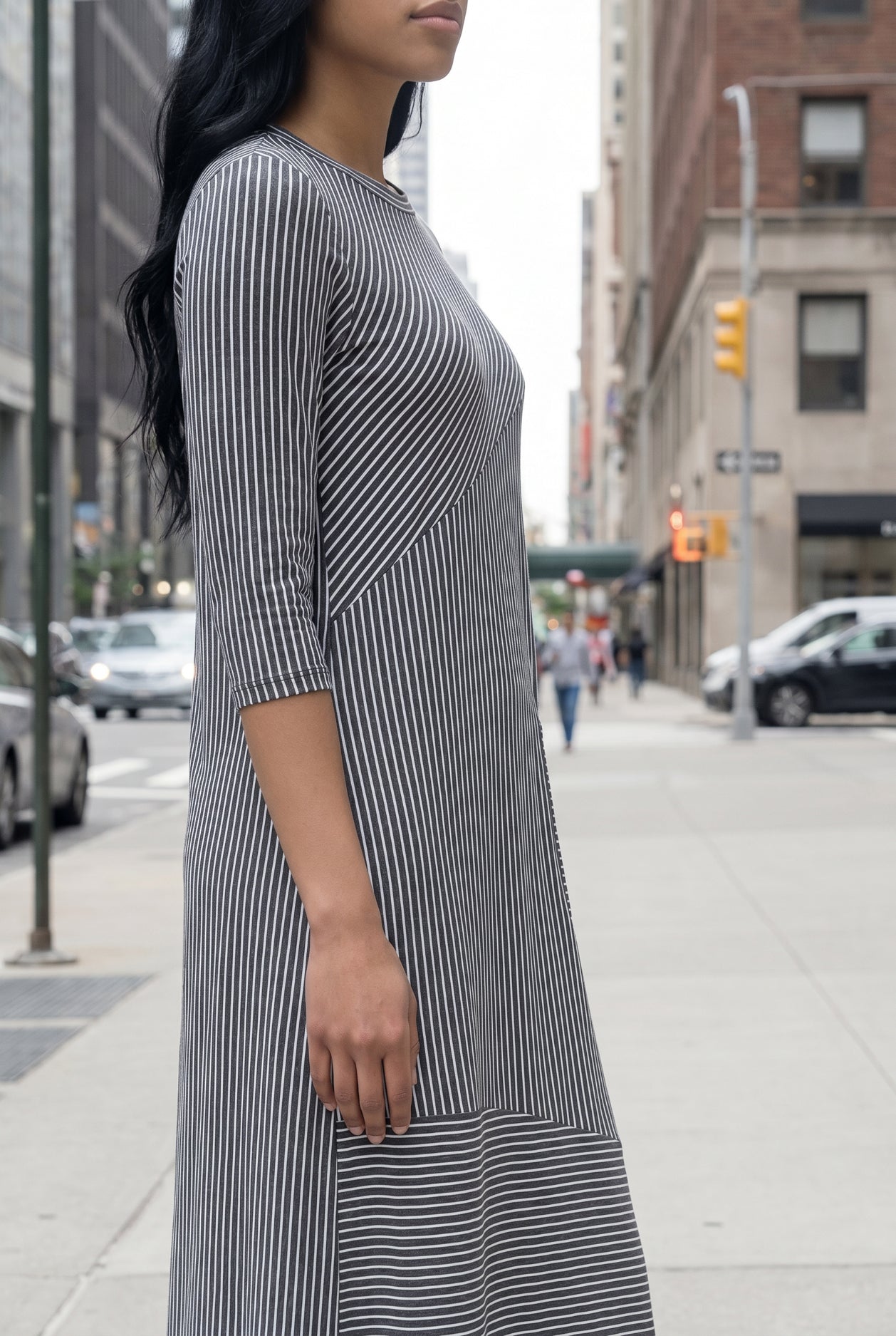 Woman in a gray dress standing on a city street with tall buildings in the background.