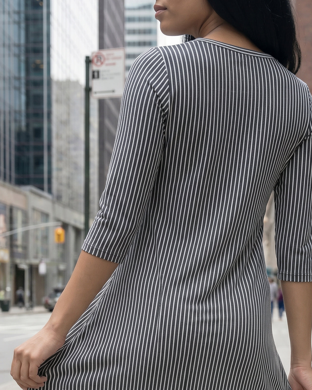 Woman in a gray dress standing on a city street with tall buildings in the background.