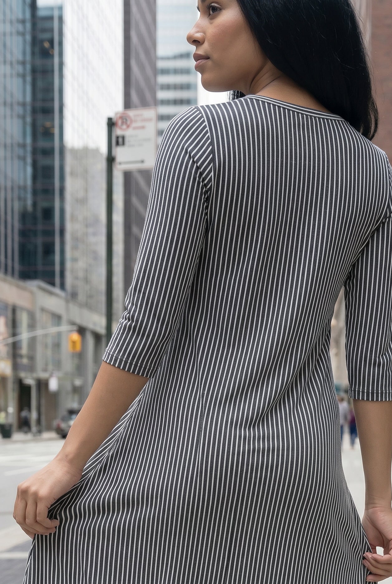 Woman in a gray dress standing on a city street with tall buildings in the background.