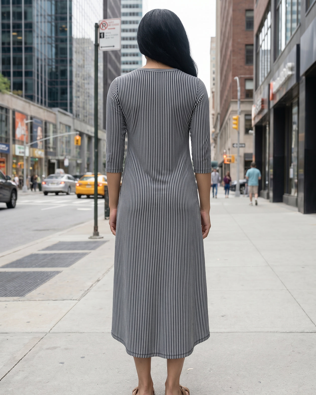 Woman in a gray dress standing on a city street with tall buildings in the background.