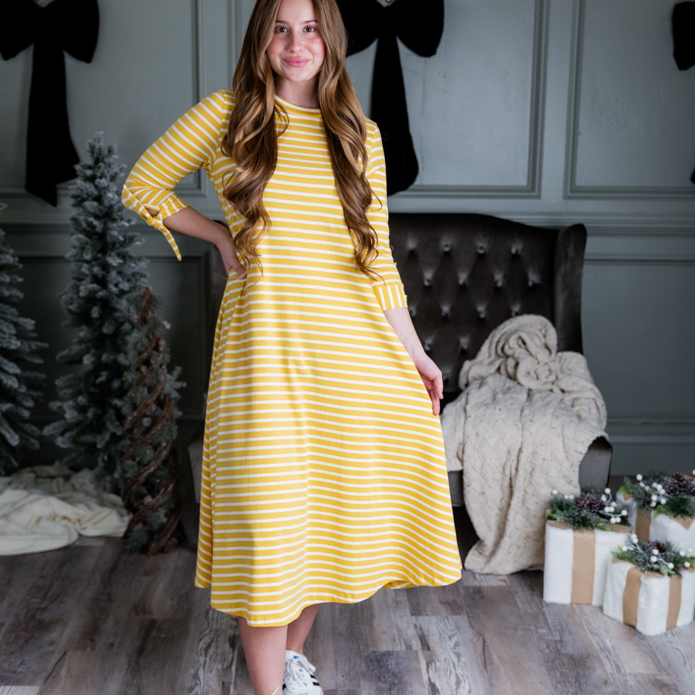 Model wearing the Nuggles® Gracie Dress, a modest A-line midi dress with ¾ sleeves and tie accents, made from soft knit fabric.