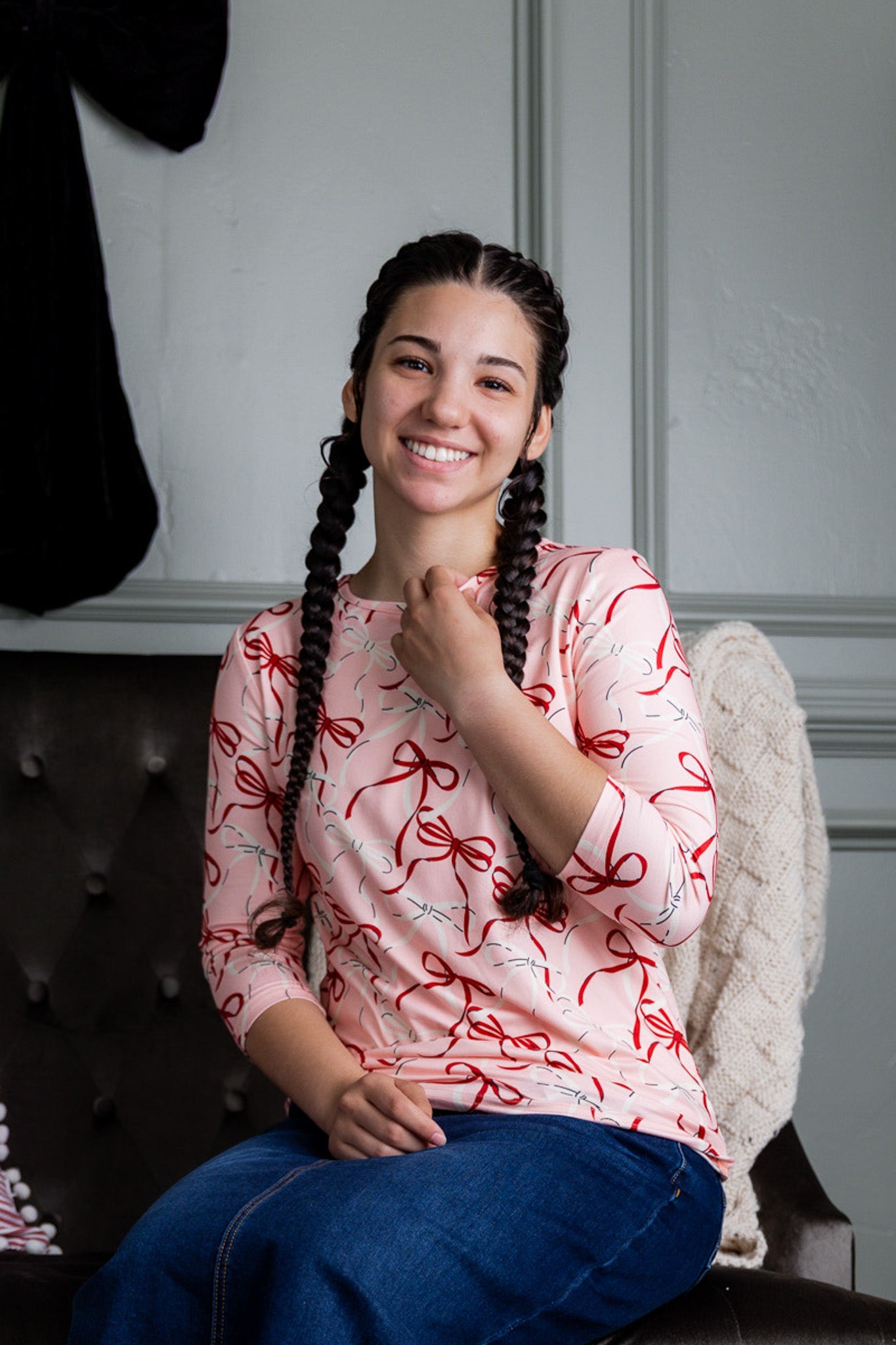 Woman with braided hair wearing a pink shirt with red patterns, sitting on a couch.