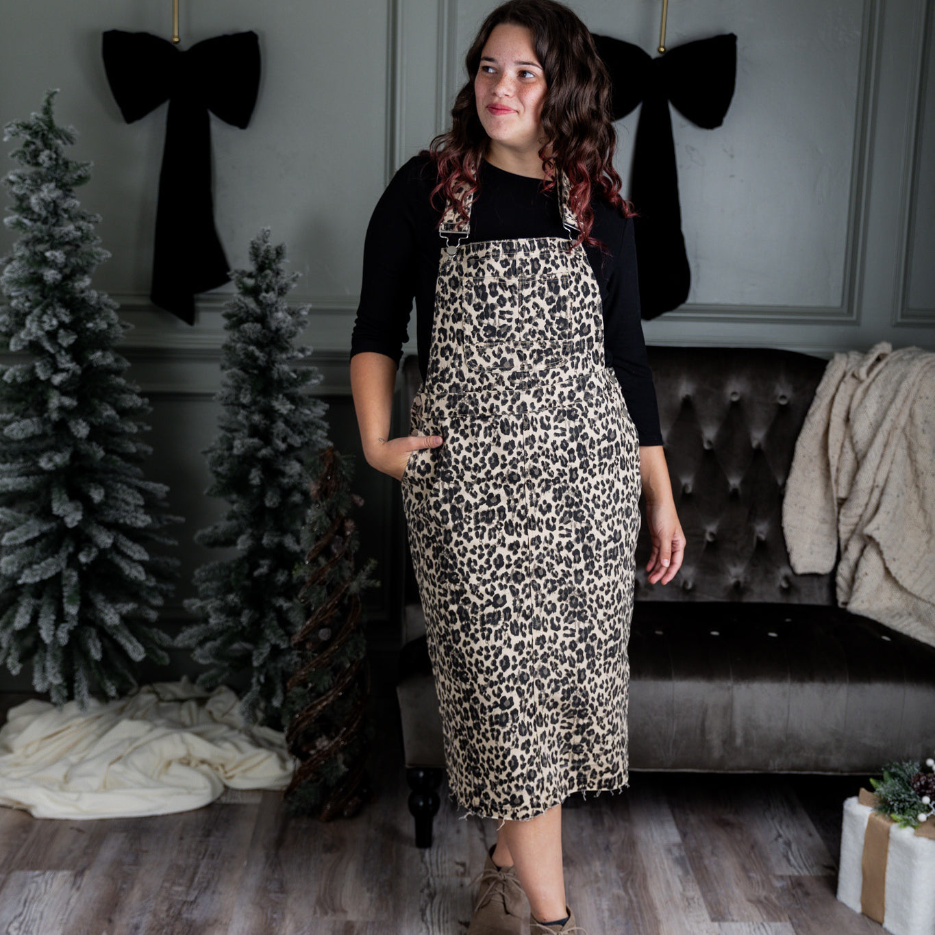 Model wearing a 'NUGGLES® modest dark wash denim overall dress with front pocket and raw hem.