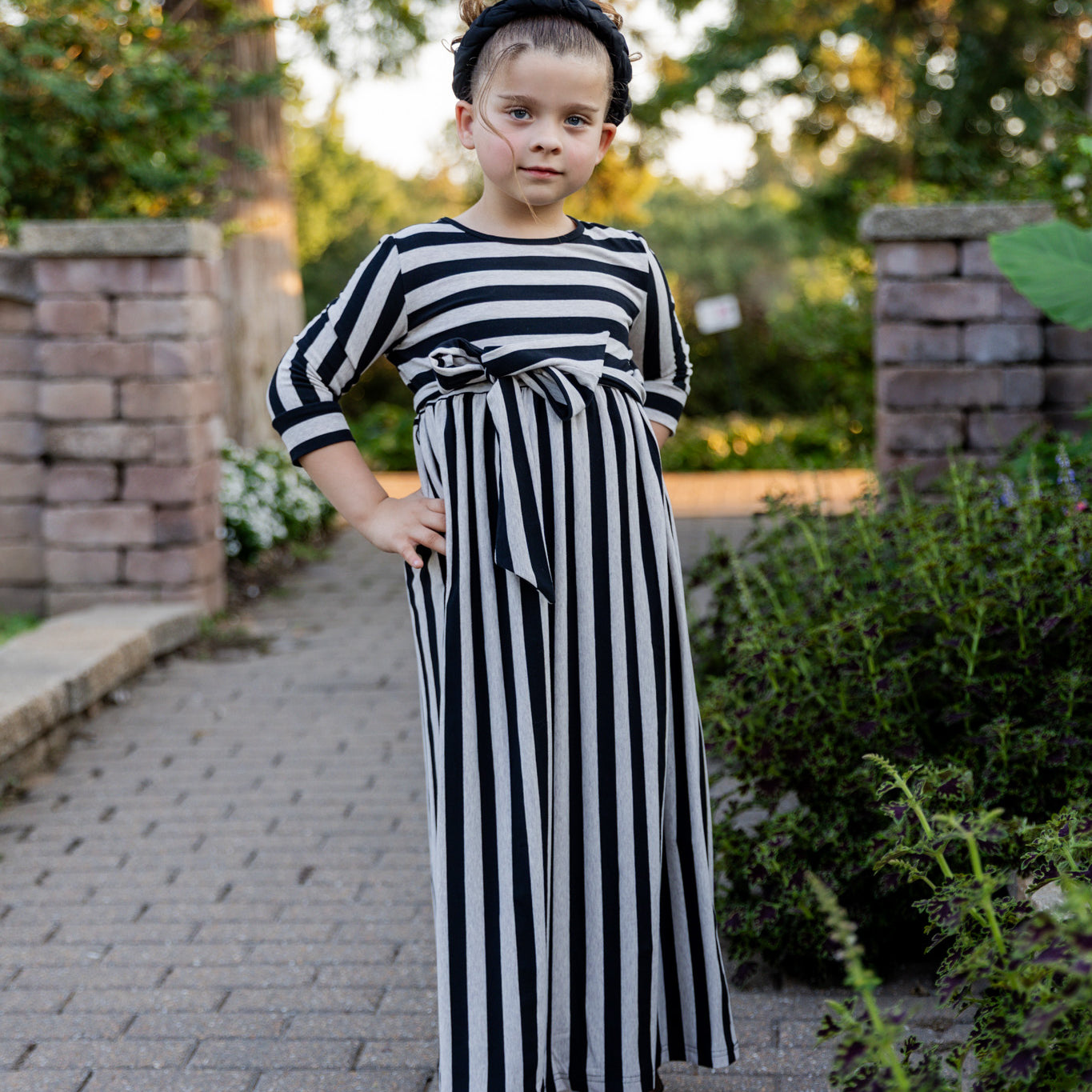 Young girl wearing the Nuggles® Girls Adelia Dress — a modest striped maxi dress with bow tie waist.