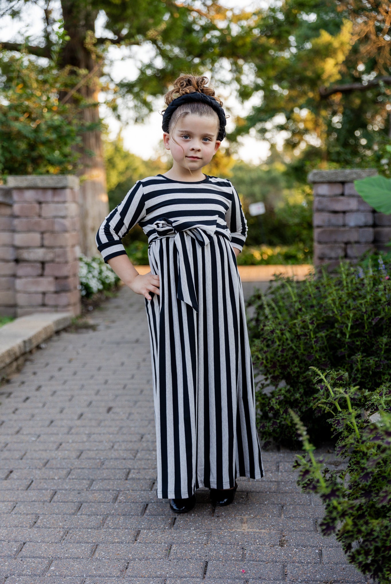 Young girl wearing the Nuggles® Girls Adelia Dress — a modest striped maxi dress with bow tie waist.
