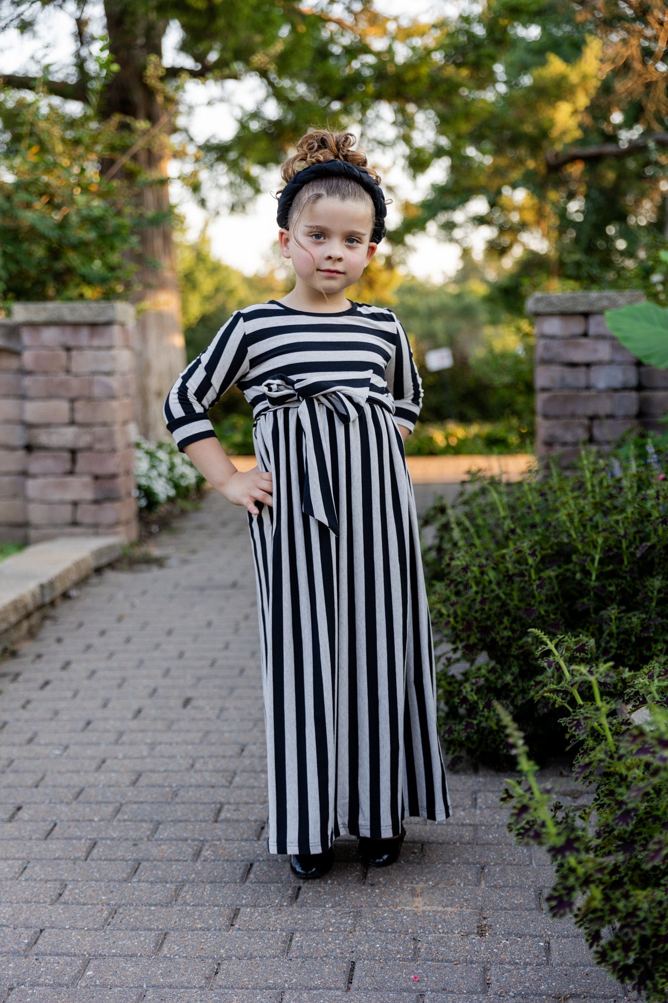 Young girl wearing the Nuggles® Girls Adelia Dress — a modest striped maxi dress with bow tie waist.