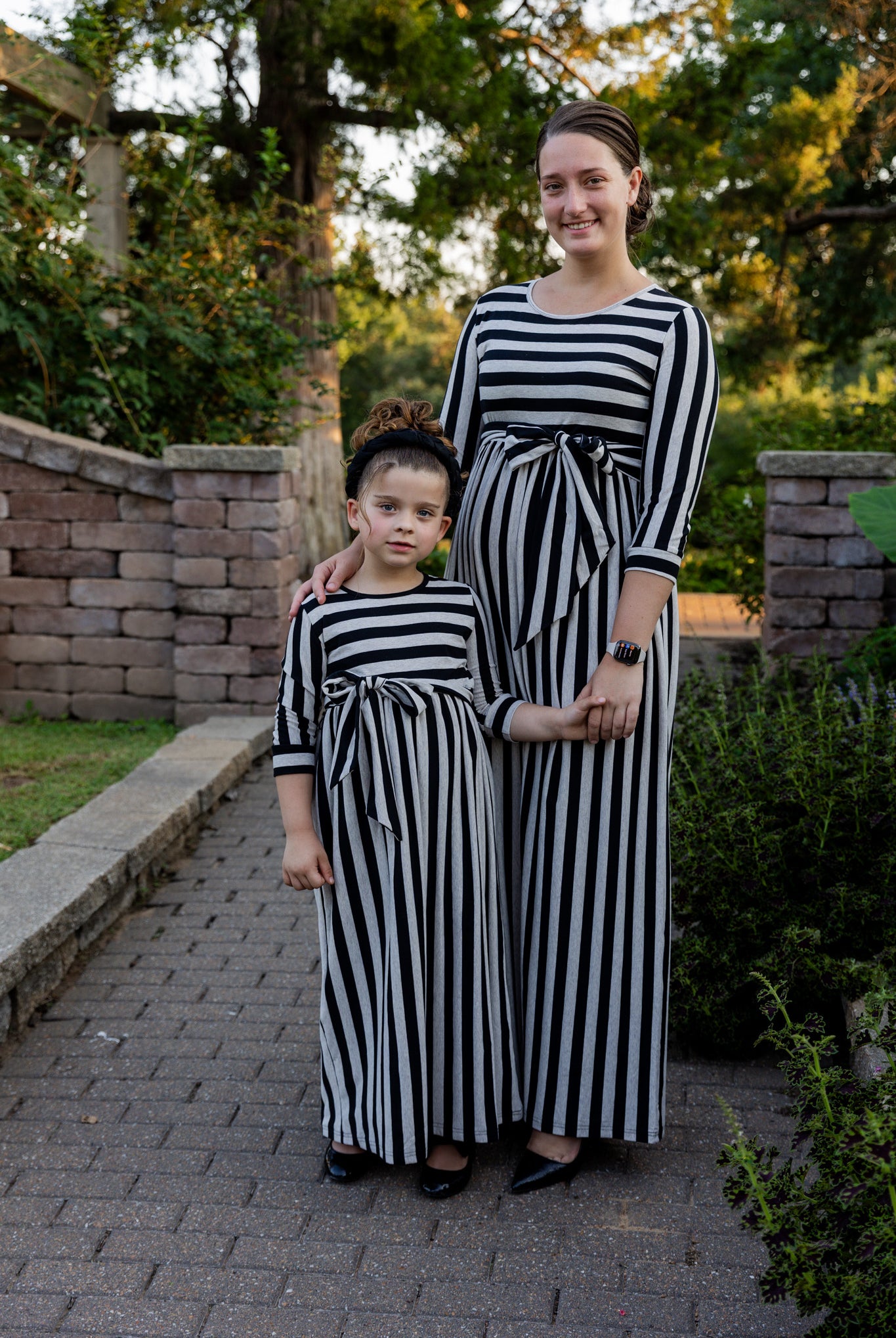 Young girl wearing the Nuggles® Girls Adelia Dress — a modest striped maxi dress with bow tie waist.