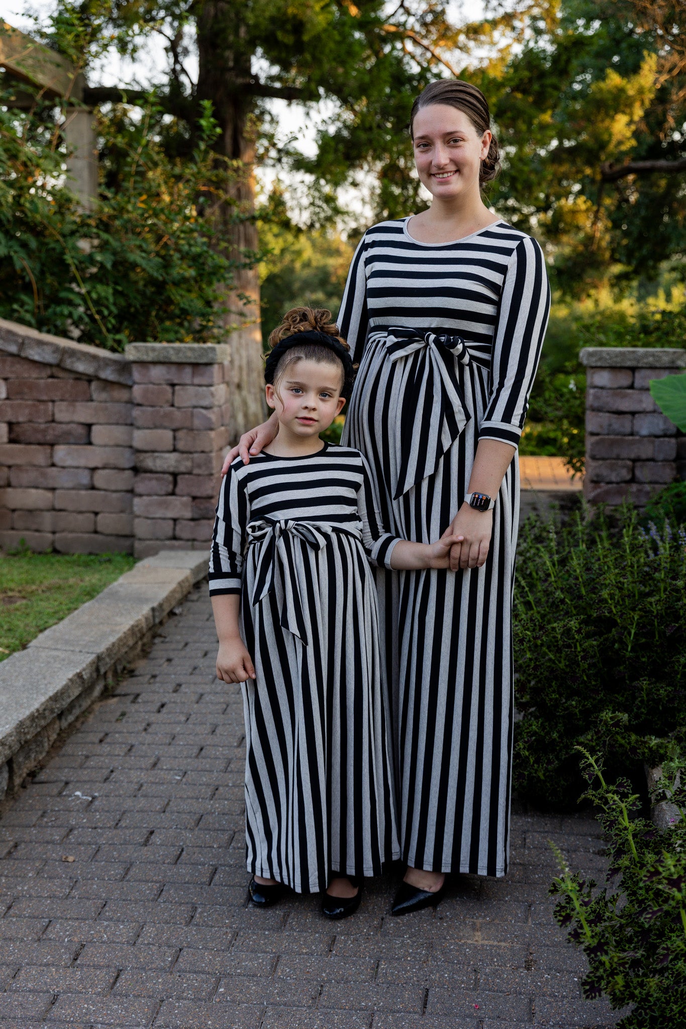 Young girl wearing the Nuggles® Girls Adelia Dress — a modest striped maxi dress with bow tie waist.