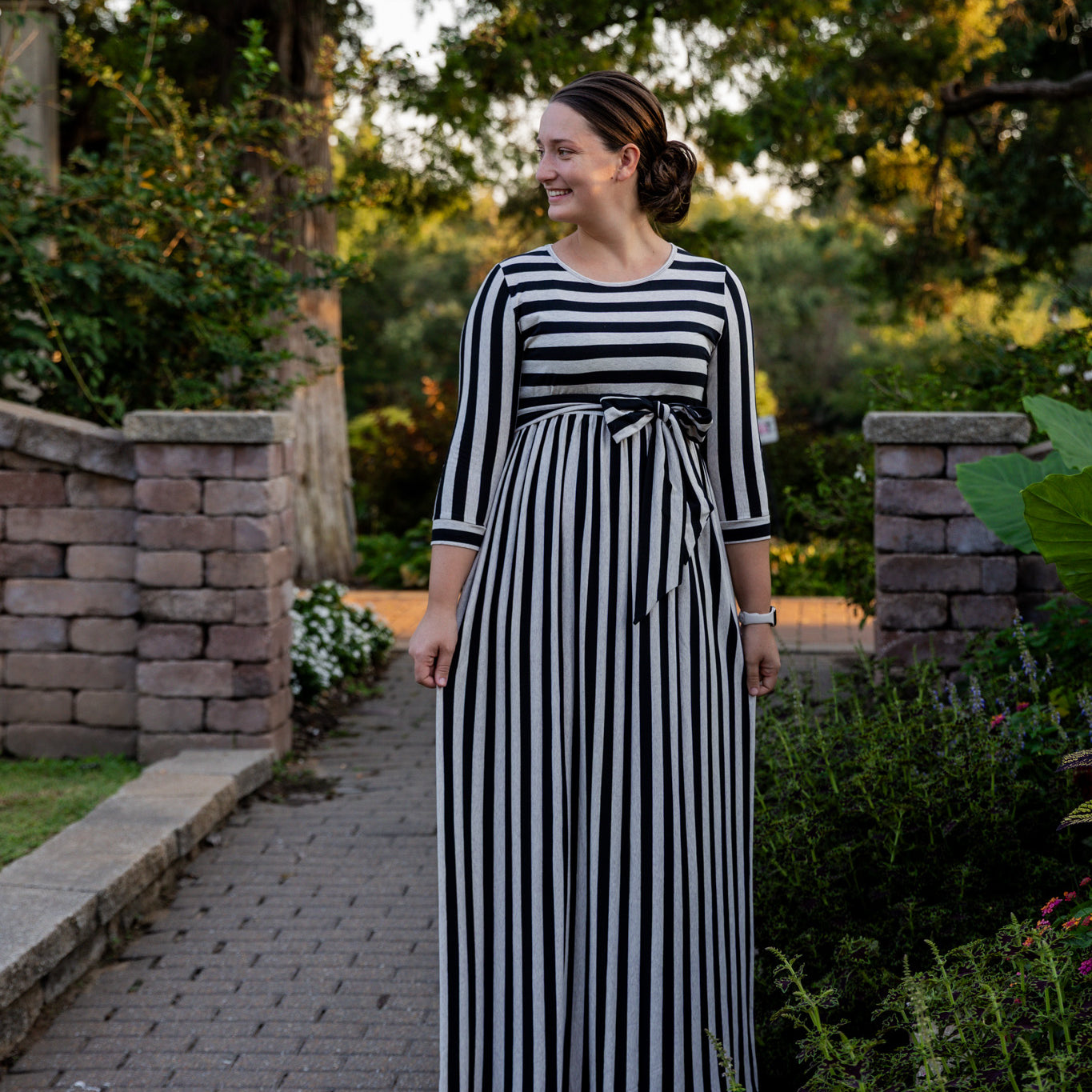 Model wearing the Nuggles® Adelia Dress, a modest striped maxi dress with waist tie and ¾ sleeves.