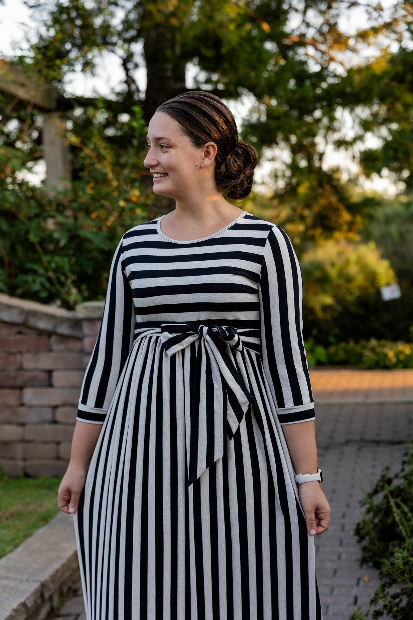 Model wearing the Nuggles® Adelia Dress, a modest striped maxi dress with waist tie and ¾ sleeves.