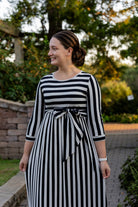 Model wearing the Nuggles® Adelia Dress, a modest striped maxi dress with waist tie and ¾ sleeves.