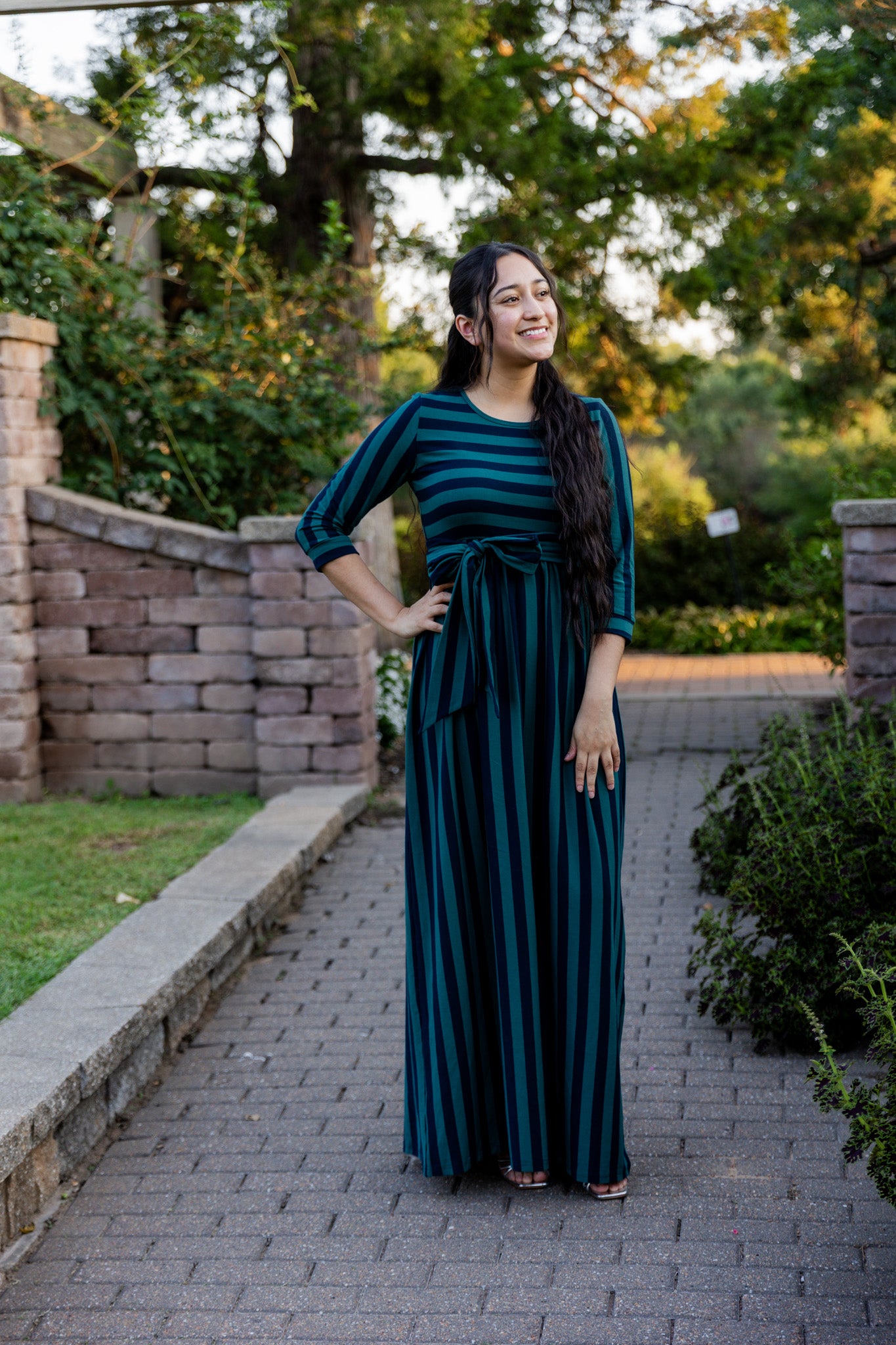 Model wearing the Nuggles® Adelia Dress, a modest striped maxi dress with waist tie and ¾ sleeves.