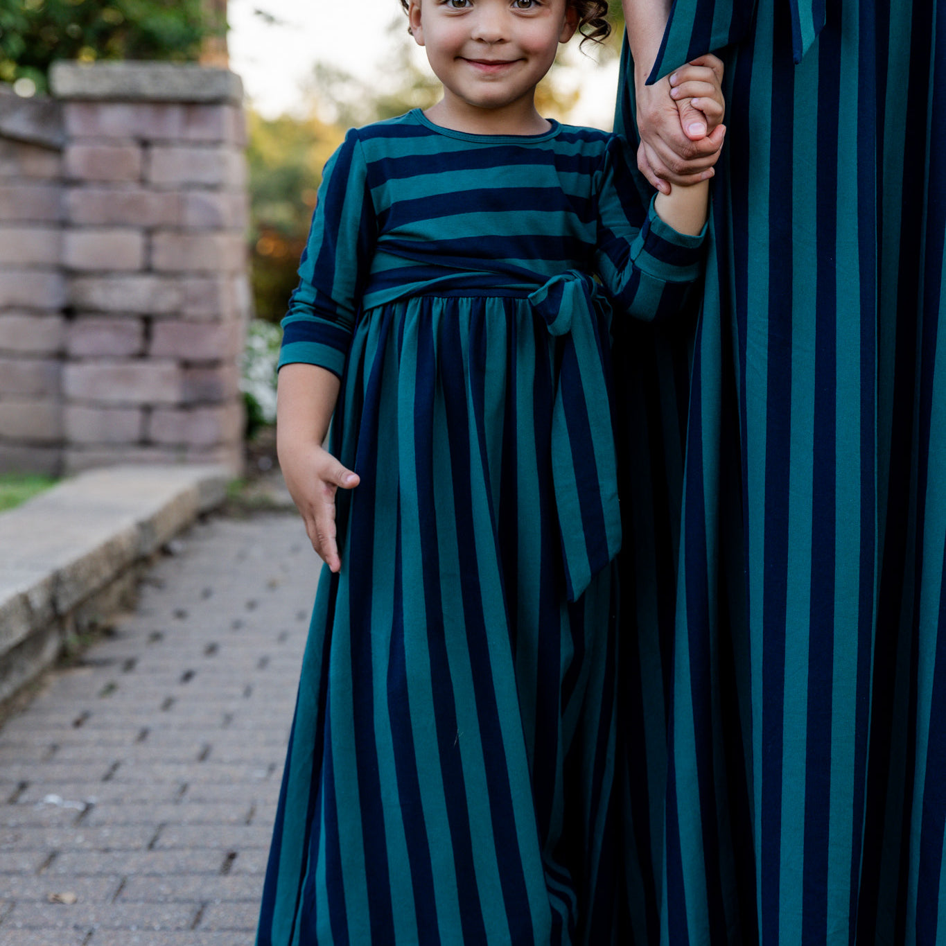 Young girl wearing the Nuggles® Girls Adelia Dress — a modest striped maxi dress with bow tie waist.
