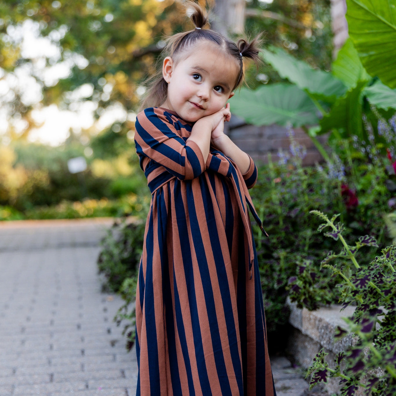 Young girl wearing the Nuggles® Girls Adelia Dress — a modest striped maxi dress with bow tie waist.